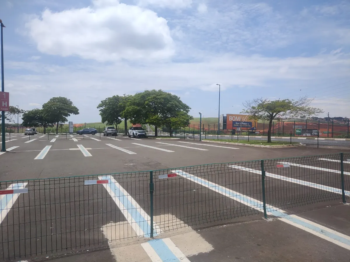 Estacionamento descoberto do shopping antes da obra, com as vagas pintadas e árvores ao fundo