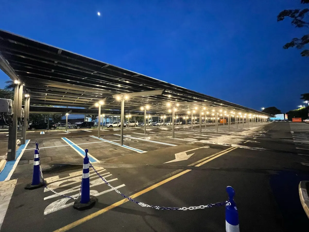 Carport solar de um shopping ao anoitecer, com a cobertura de painéis acesa sobre o estacionamento