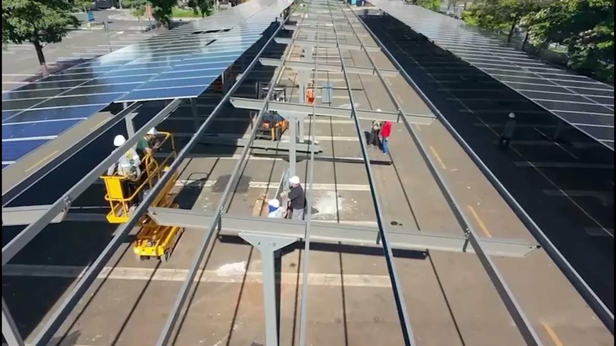 Estrutura metálica do carport vista de drone durante a montagem, com parte dos painéis solares já instalada
