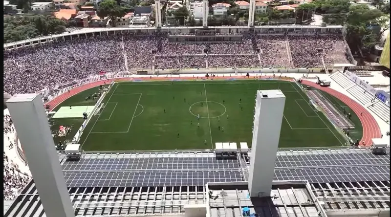 Painéis solares na cobertura da arquibancada de um estádio, com o campo e a torcida ao fundo
