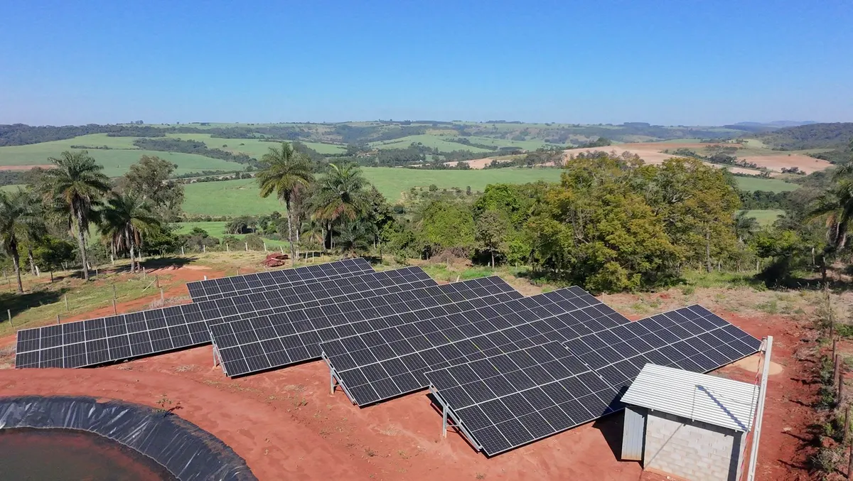 Usina solar em solo em terreno de terra vermelha, com mata e campo ao fundo