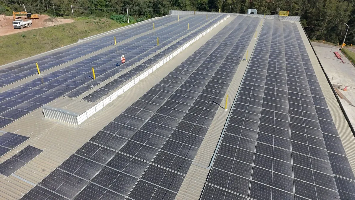Telhado comprido de galpão da Veolia coberto de painéis solares, com terreno de terra ao lado