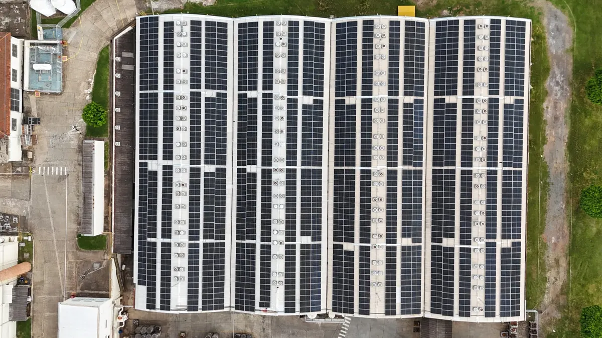 Telhado de galpão industrial coberto de fileiras de painéis solares, visto de cima