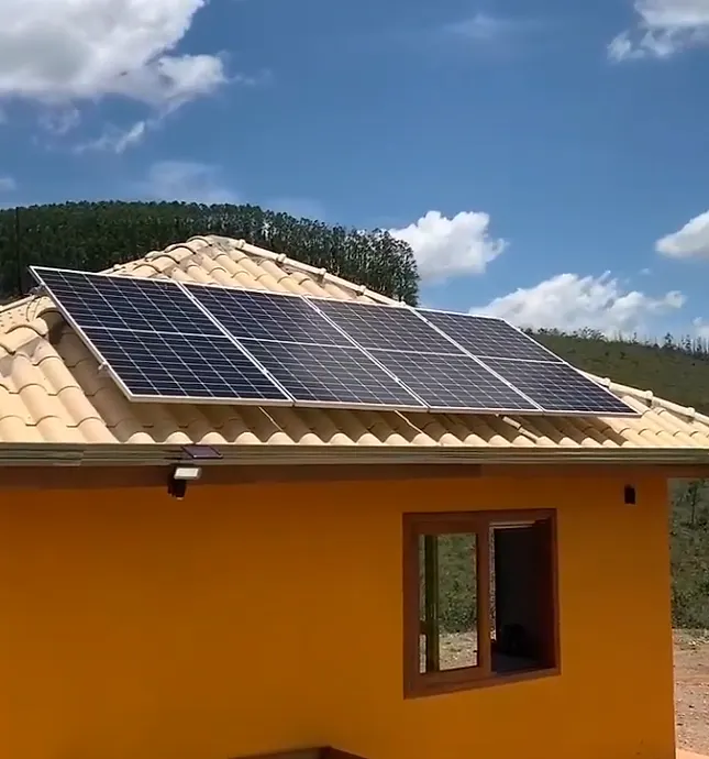 Casa de sítio com módulos solares no telhado de telha cerâmica, com morro e eucaliptos ao fundo