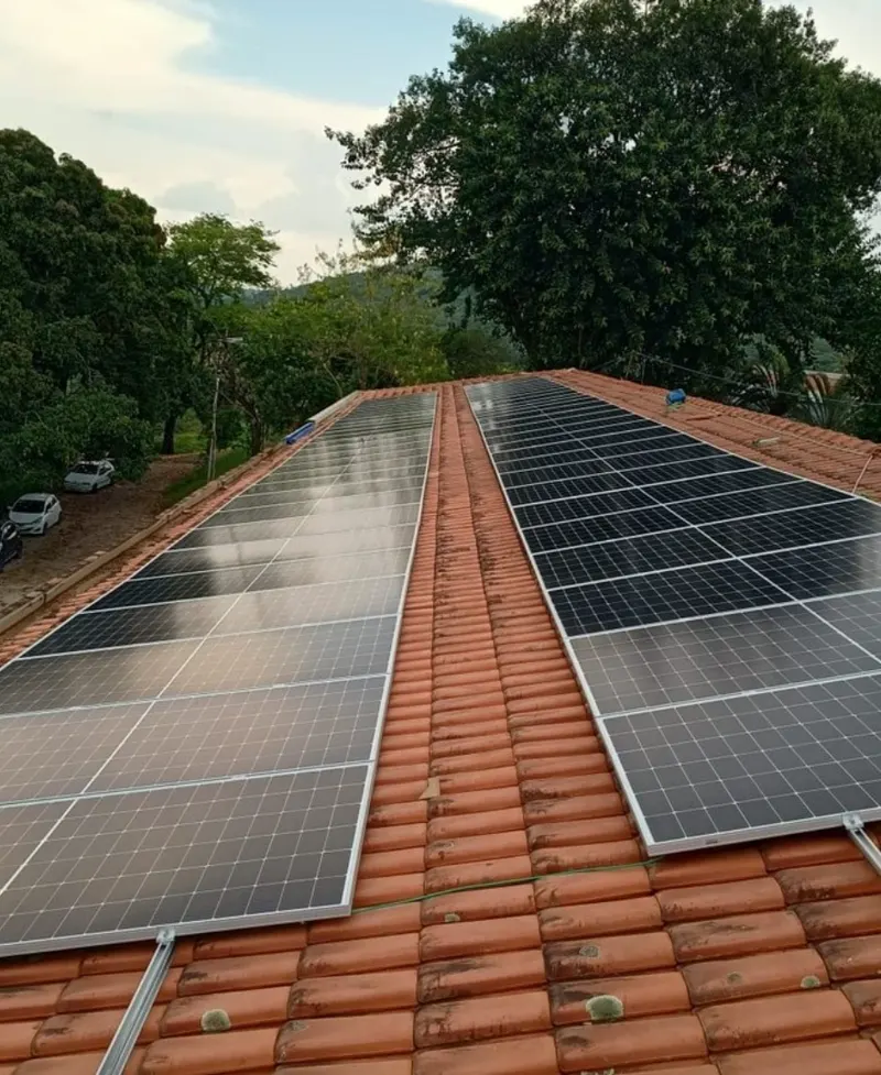 Usina solar residencial em duas águas de telhado cerâmico, com as árvores do quintal ao fundo